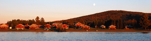 The light from a setting sun shines across Wallace Pond (Lake Wallace) warming Jackson's Lodge and Log Cabins in Vermont's Northeast Kingdom