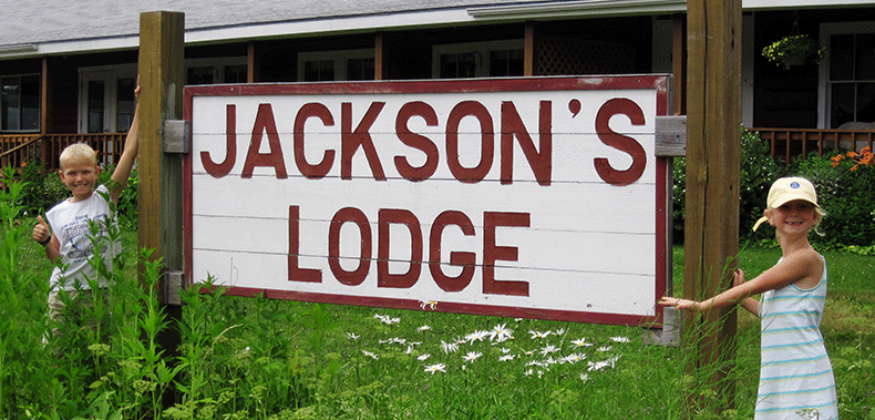 A vacationing brother and sister happily pose in front of the Jackson's Lodge sign near the main perennial garden